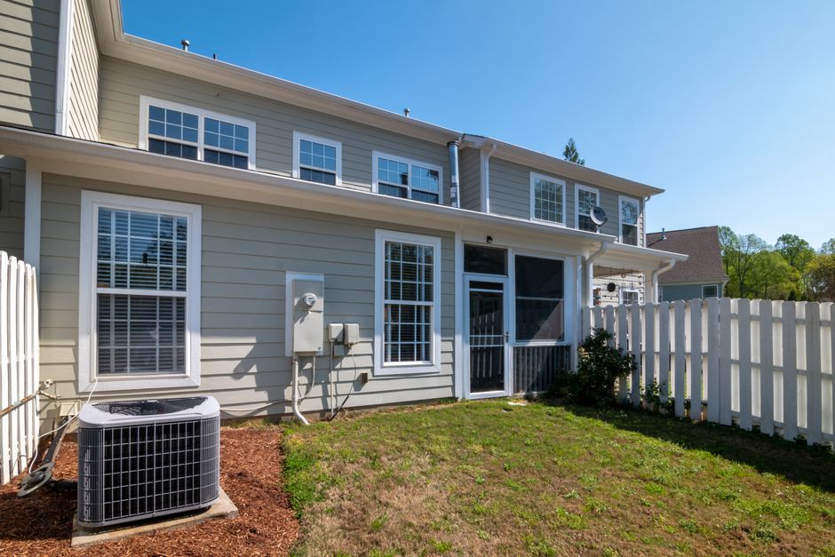 Outdoor central air conditioning condenser unit installed on a clean concrete pad next to a residential home